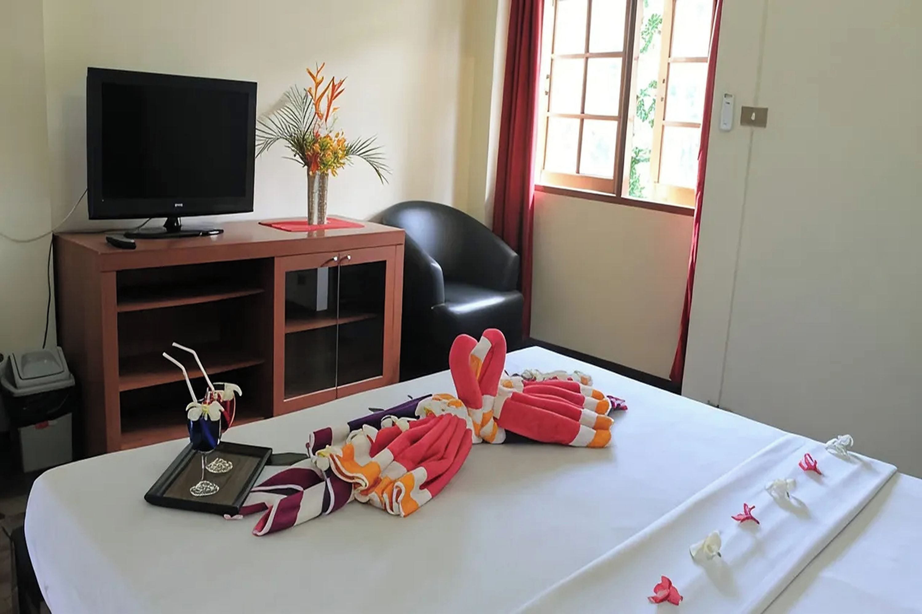 A hotel room with a bed, a TV, a desk, a chair, and a window with curtains.