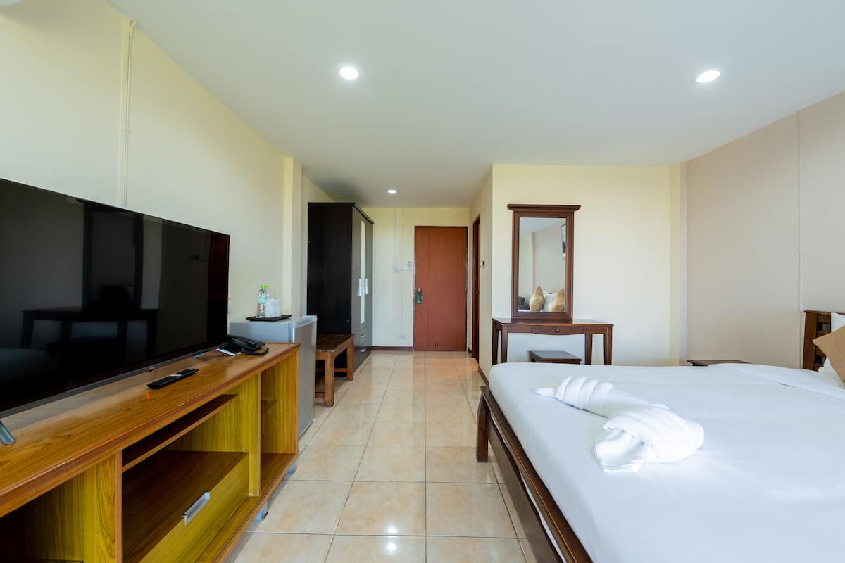 A hotel room with a TV, a desk with a phone, a bed with a towel, a mirror, and a door leading to another room.