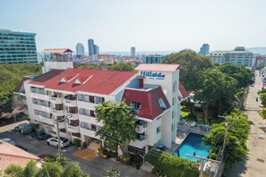 A multi-story hotel with a red roof and a swimming pool.