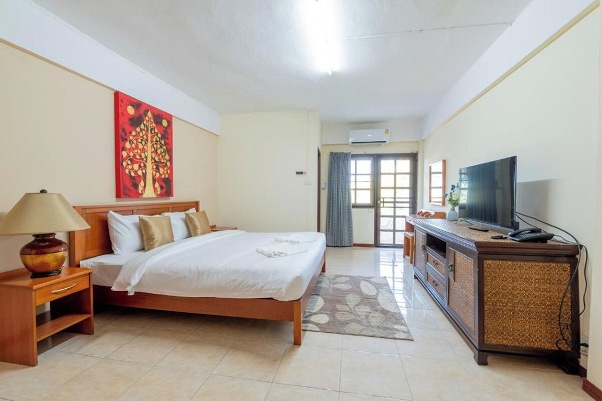 A hotel room with a bed, a television, a desk, and a painting on the wall.