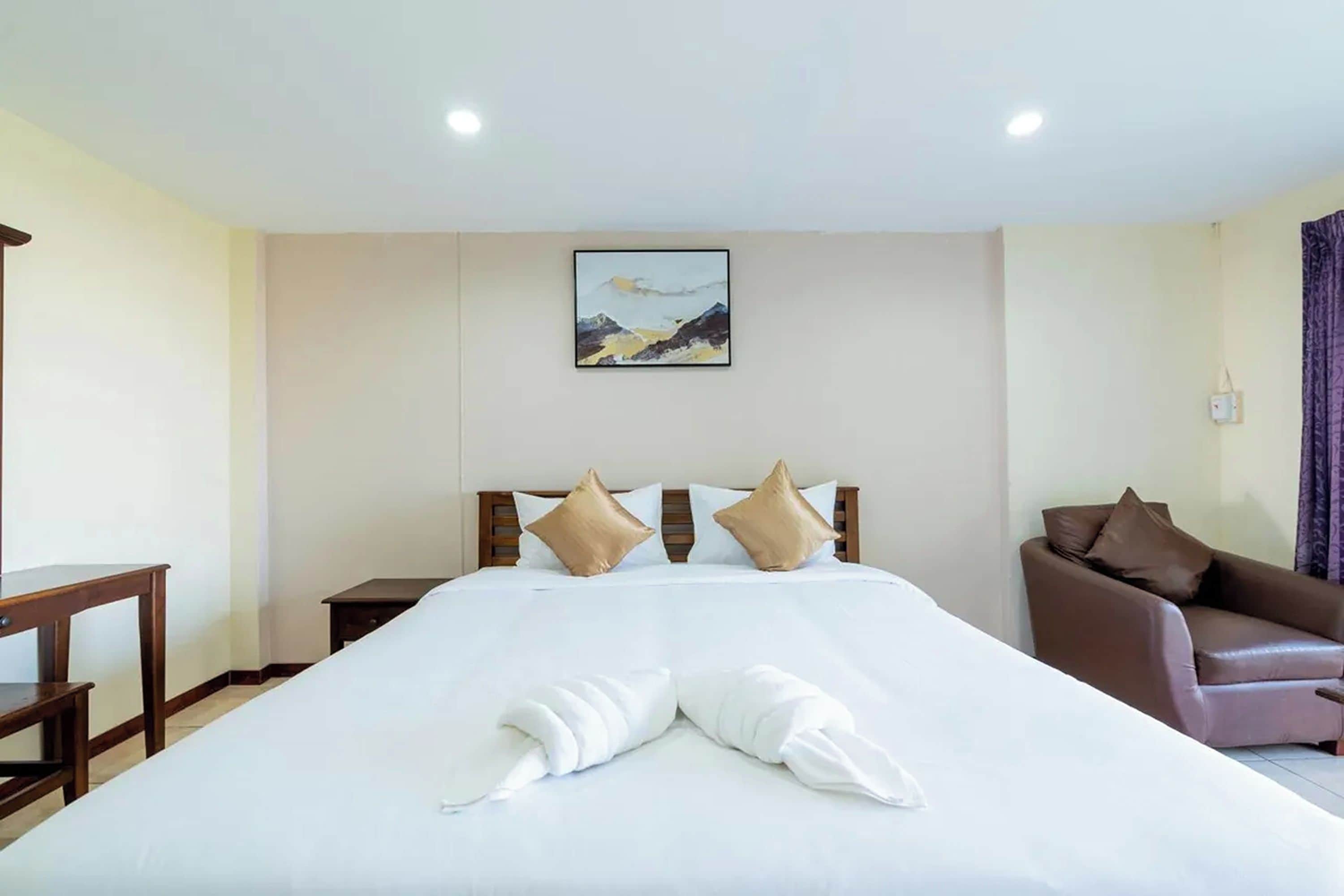 Een hotelkamer met een groot bed, een houten hoofdbord, een schilderij aan de muur, een bruine leren fauteuil en een kleine tafel.