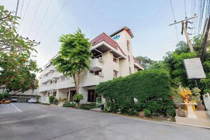 A multi-story building with a flat roof and a sign indicating a hotel. There are trees and shrubs in front, and a street with parked cars. - Hillside Resort Pattaya (Pattaya)