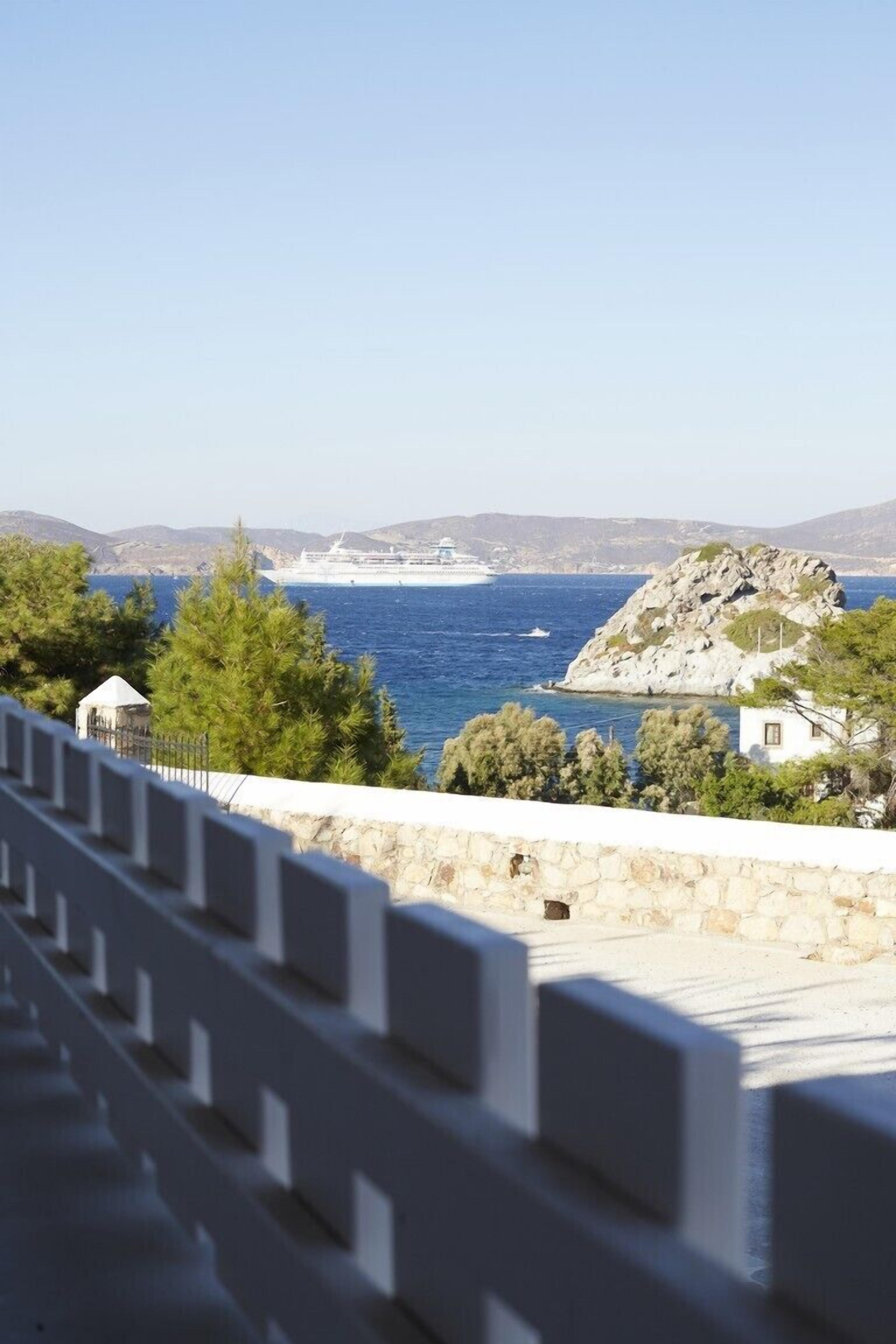 A coastal view with a rocky island, a cruise ship in the distance, and a white building with a small structure nearby.
