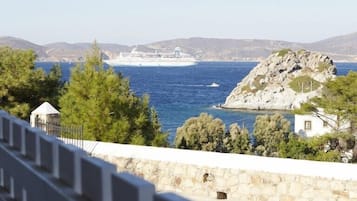 A coastal view with a rocky island, a cruise ship in the distance, and a white building with a small structure nearby.