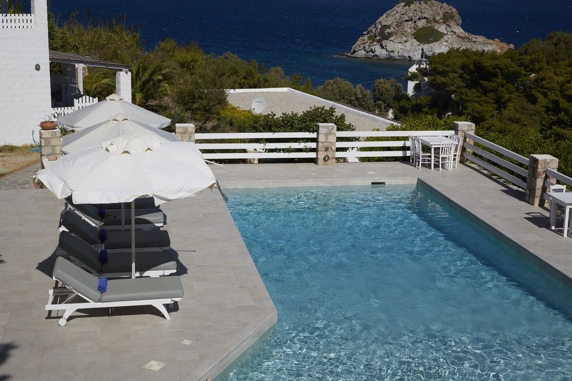 Un espace piscine avec des chaises longues et des parasols, une clôture blanche et une vue sur la mer et le paysage rocheux.