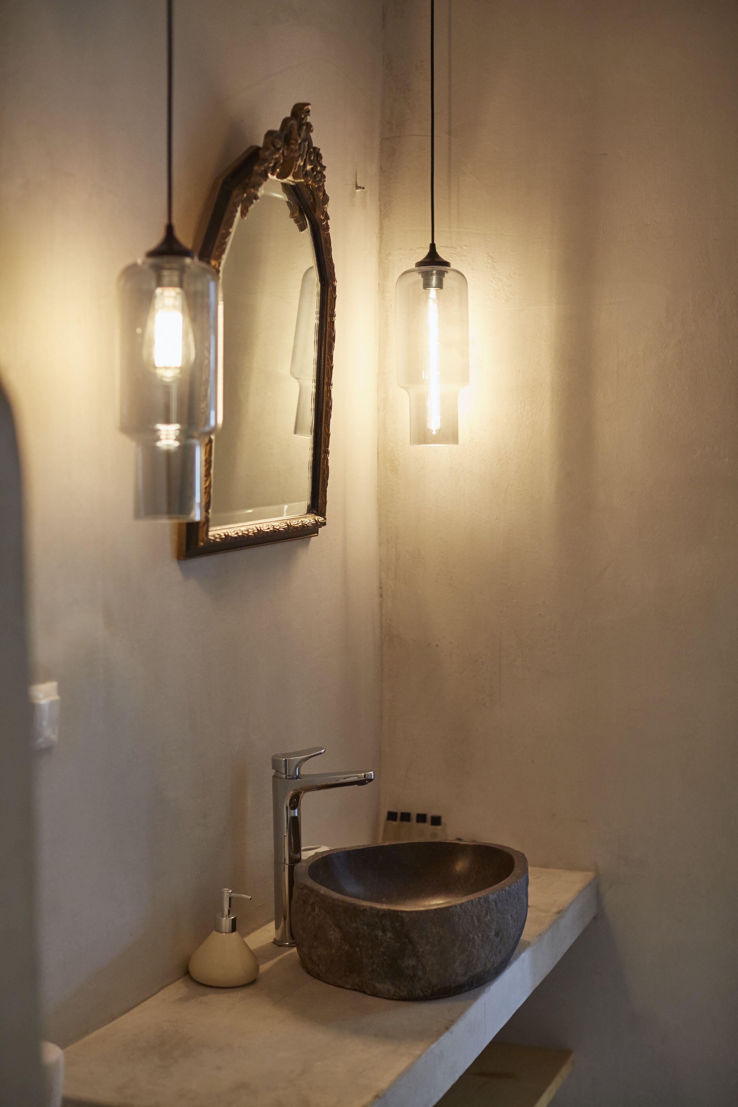 Een badkamer met een wastafel van steen, een spiegel met een versierd omlijsting en twee hanglampen.