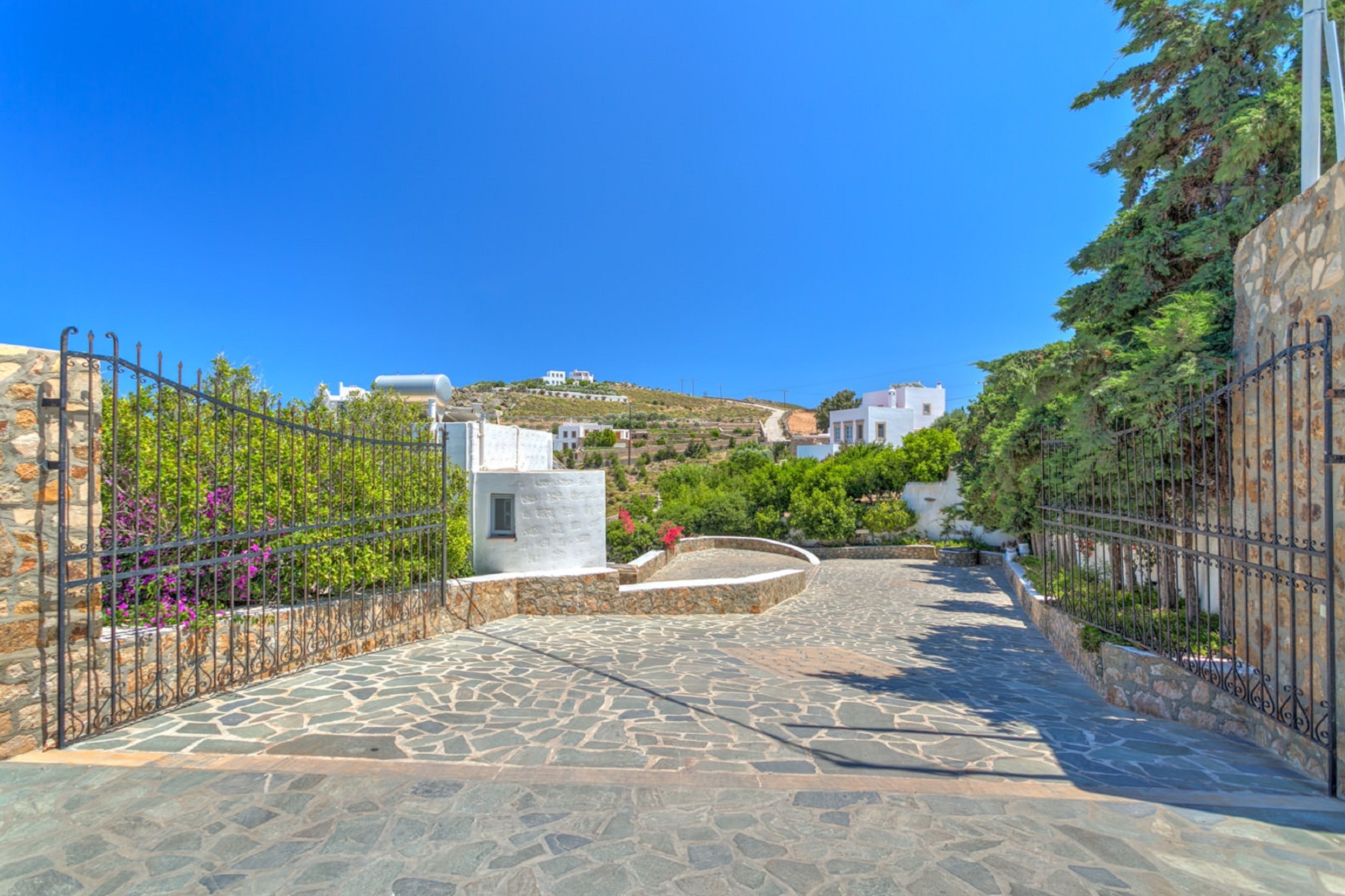 A stone-paved pathway leading to a white building with a stone wall and metal fence on one side.