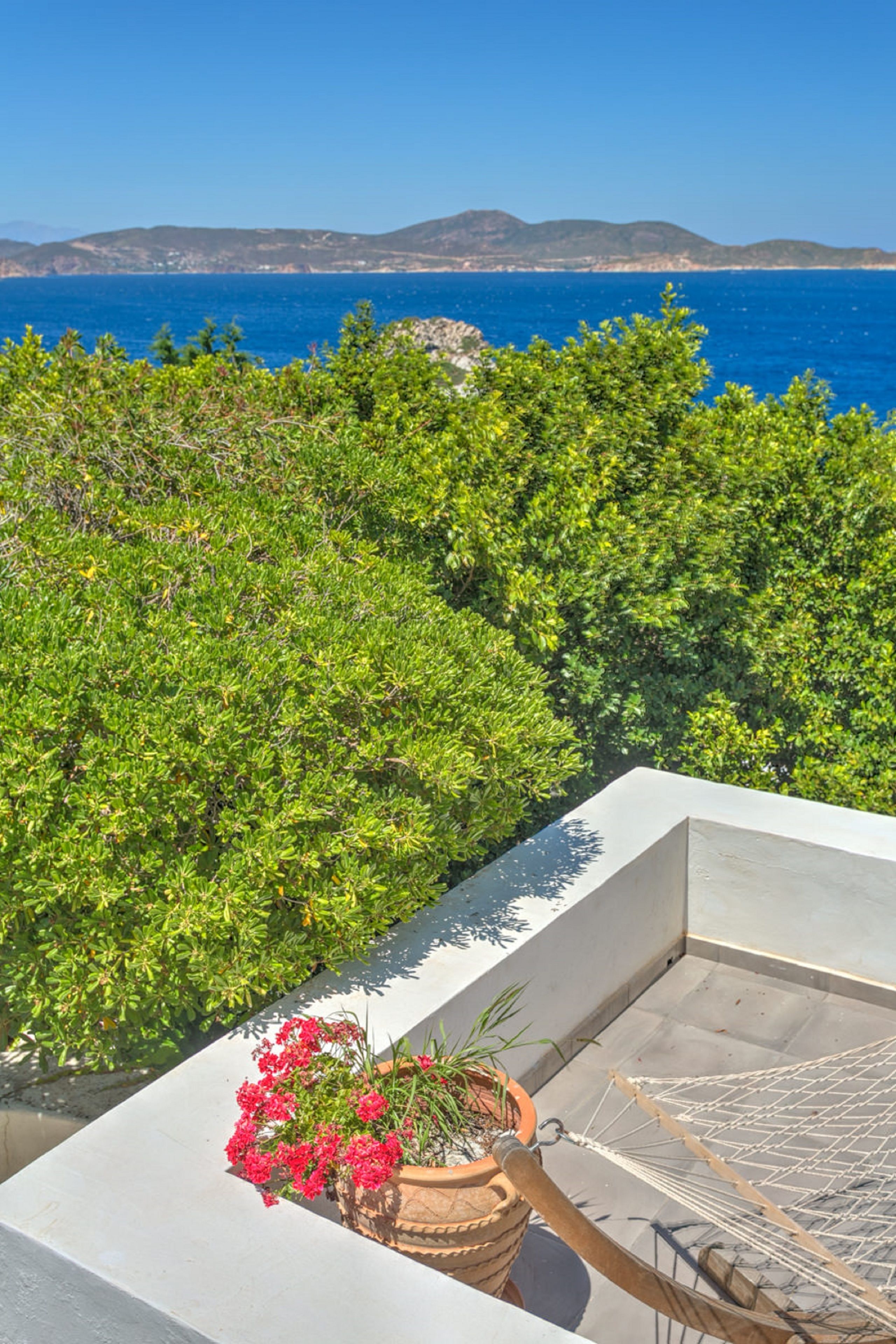 Ein Balkon mit Blick auf das Meer und die Berge, einer Hängematte und einem Blumentopf mit Blumen.