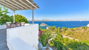 A terrace with a pergola, outdoor seating, and a view of the sea and distant hills.