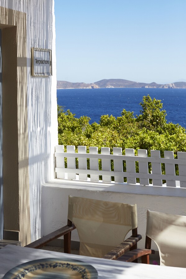 A terrace with a white fence, two chairs, and a view of the sea and distant hills.