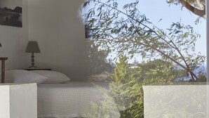A bedroom with a bed, a nightstand, a lamp, and a window overlooking greenery.