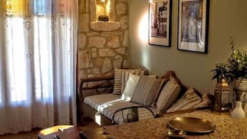 Una sala de estar acogedora con una pared de piedra, un sofá con cojines a rayas, una mesa con mantel de encaje y dos cuadros en la pared.