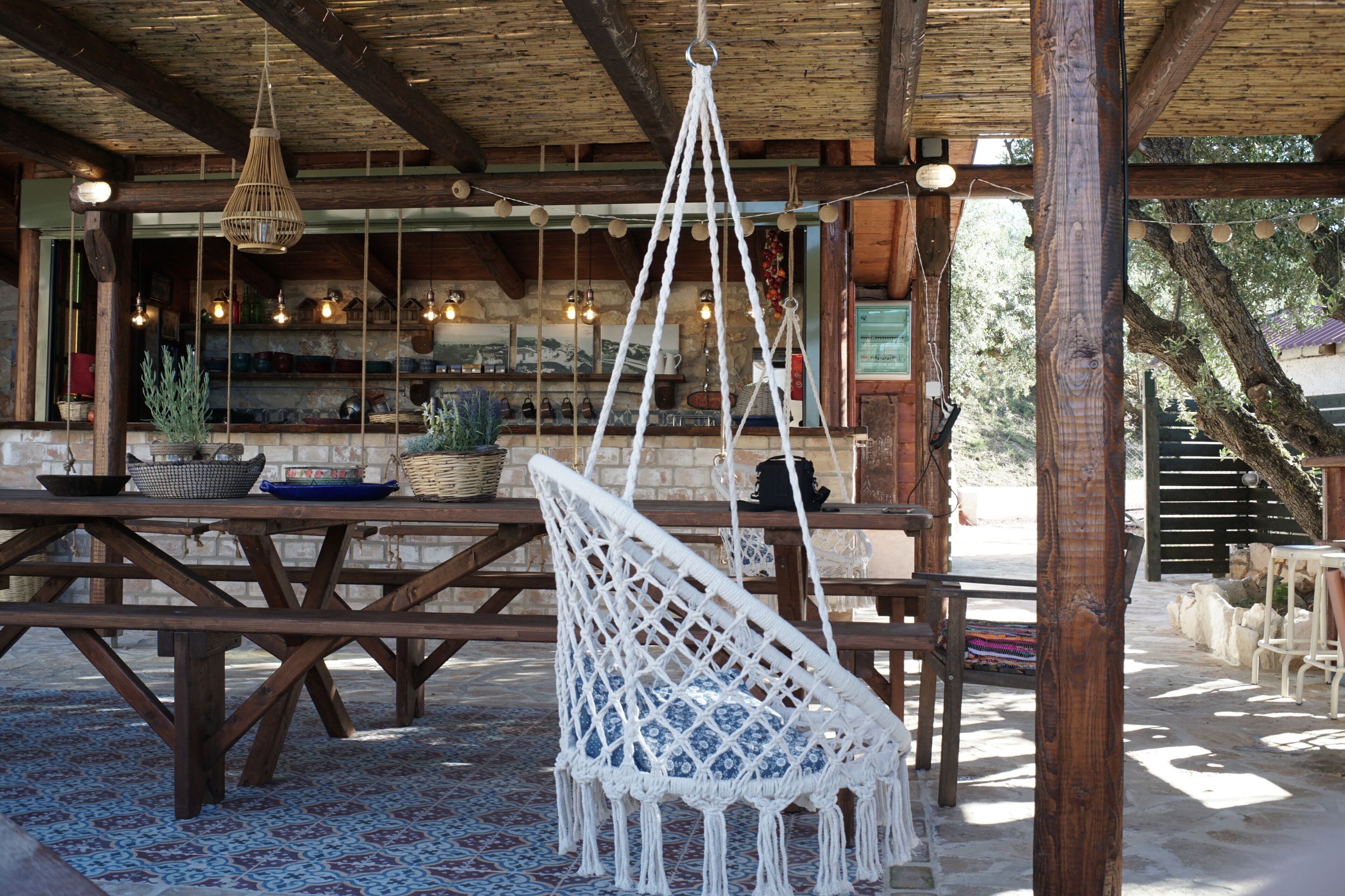 A rustic outdoor seating area with wooden tables and a hanging macrame chair.