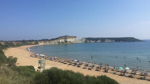A beach with umbrellas and sun loungers, a lifeguard tower, and cliffs in the background. - Alegria Villas (Zakynthos)