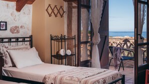 A bedroom with a bed, a small shelf, and a view of the sea. - Alegria Villas (Zakynthos)
