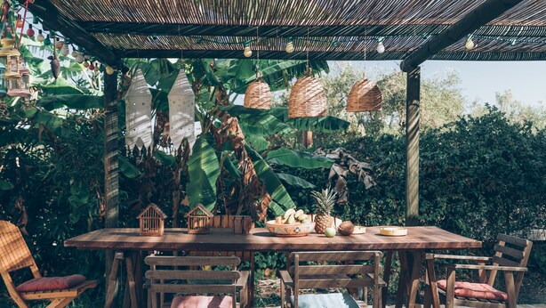 An outdoor wooden table with chairs, surrounded by lush greenery and hanging baskets. - Alegria Villas (Zakynthos)
