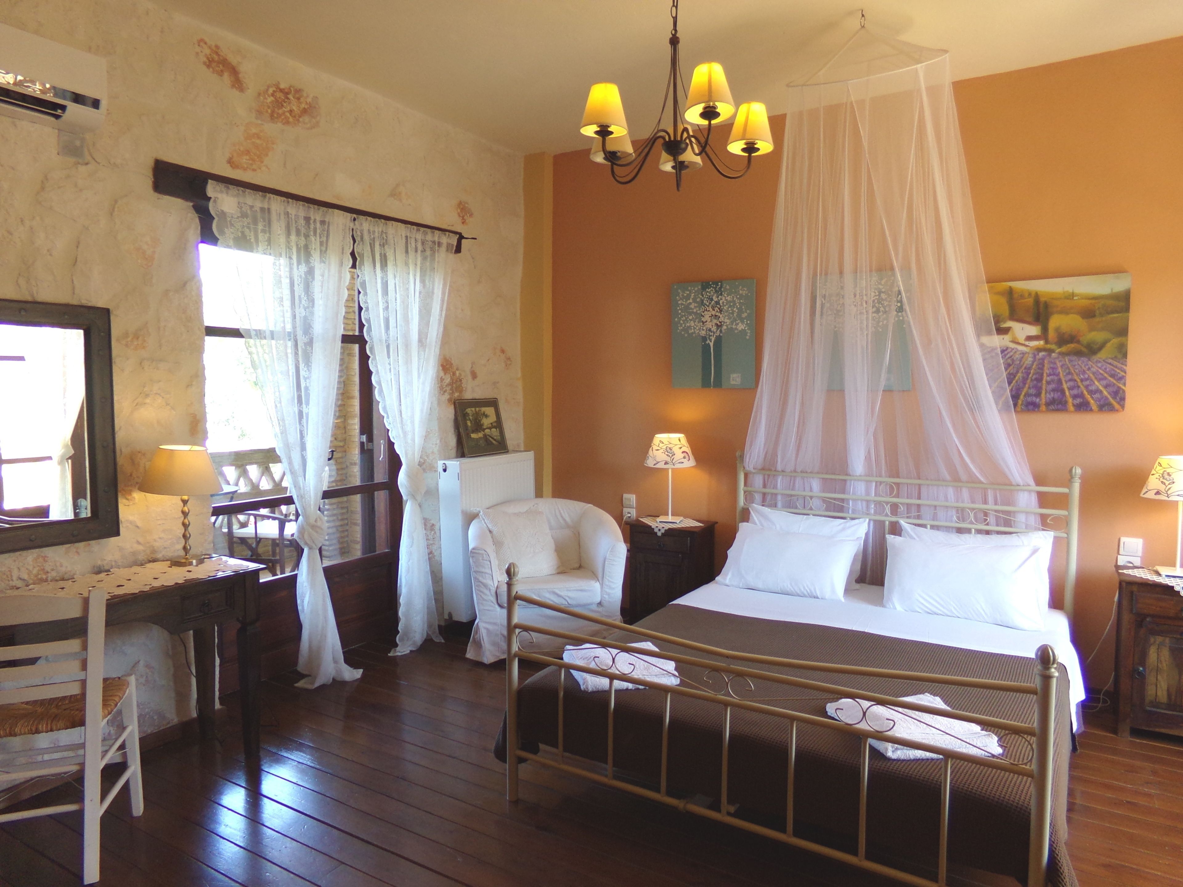 A bedroom with a four-poster bed, a wooden floor, a desk with a chair, and a window with curtains.
