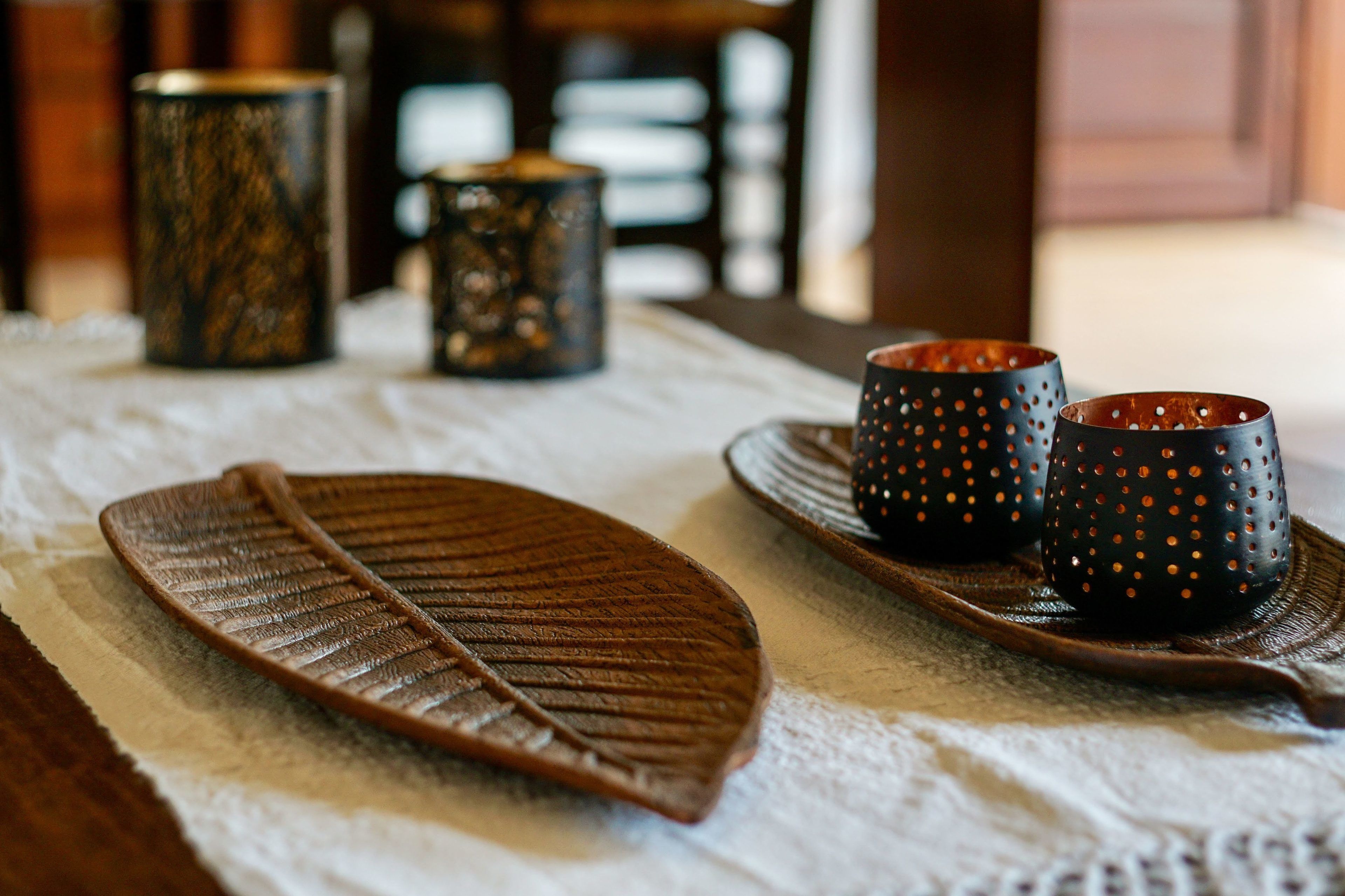 Una mesa con un posavasos con forma de hoja, dos tazas con diseño de puntos y un recipiente cilíndrico.