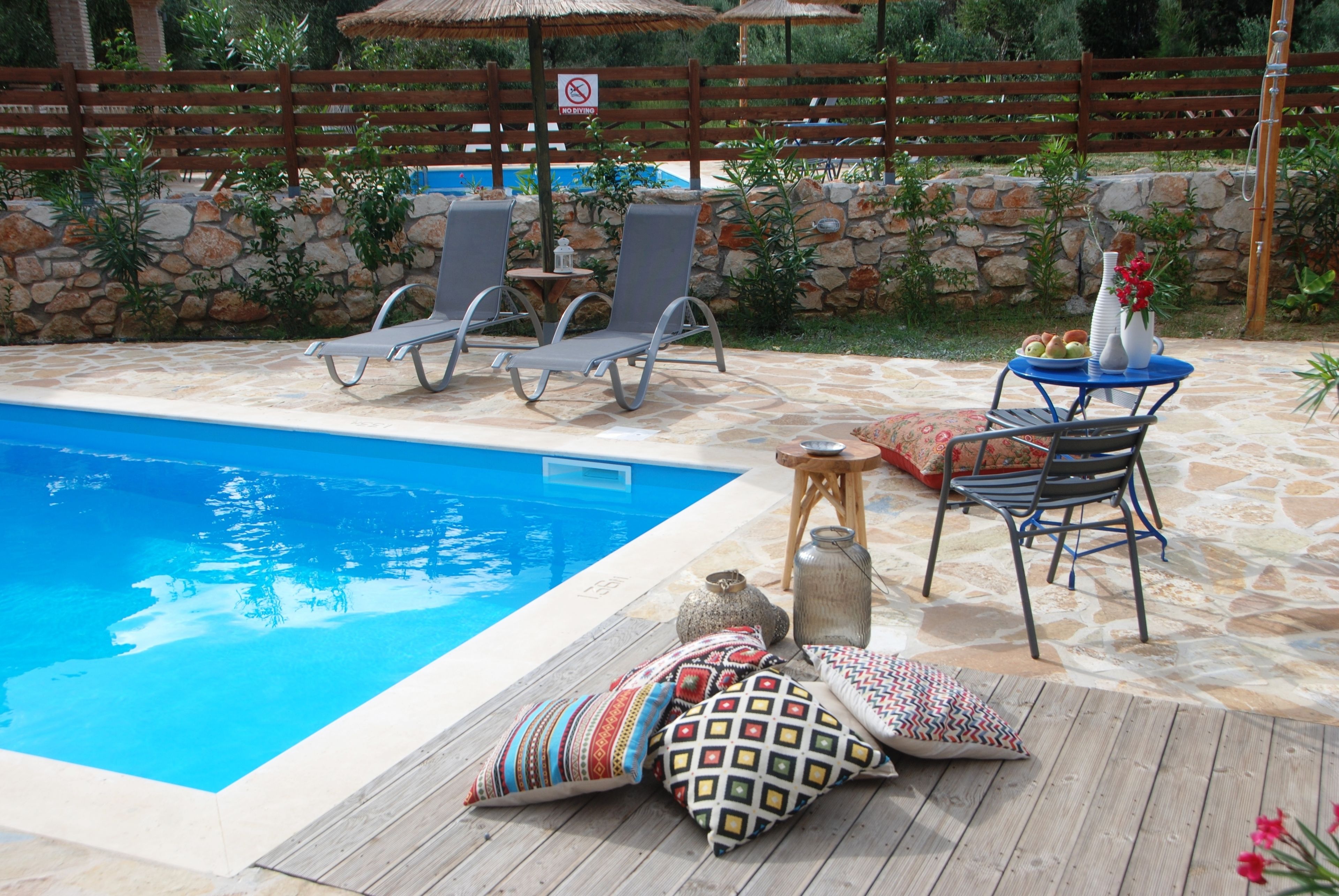 A poolside area with lounge chairs, a table with a vase, and a stone wall.
