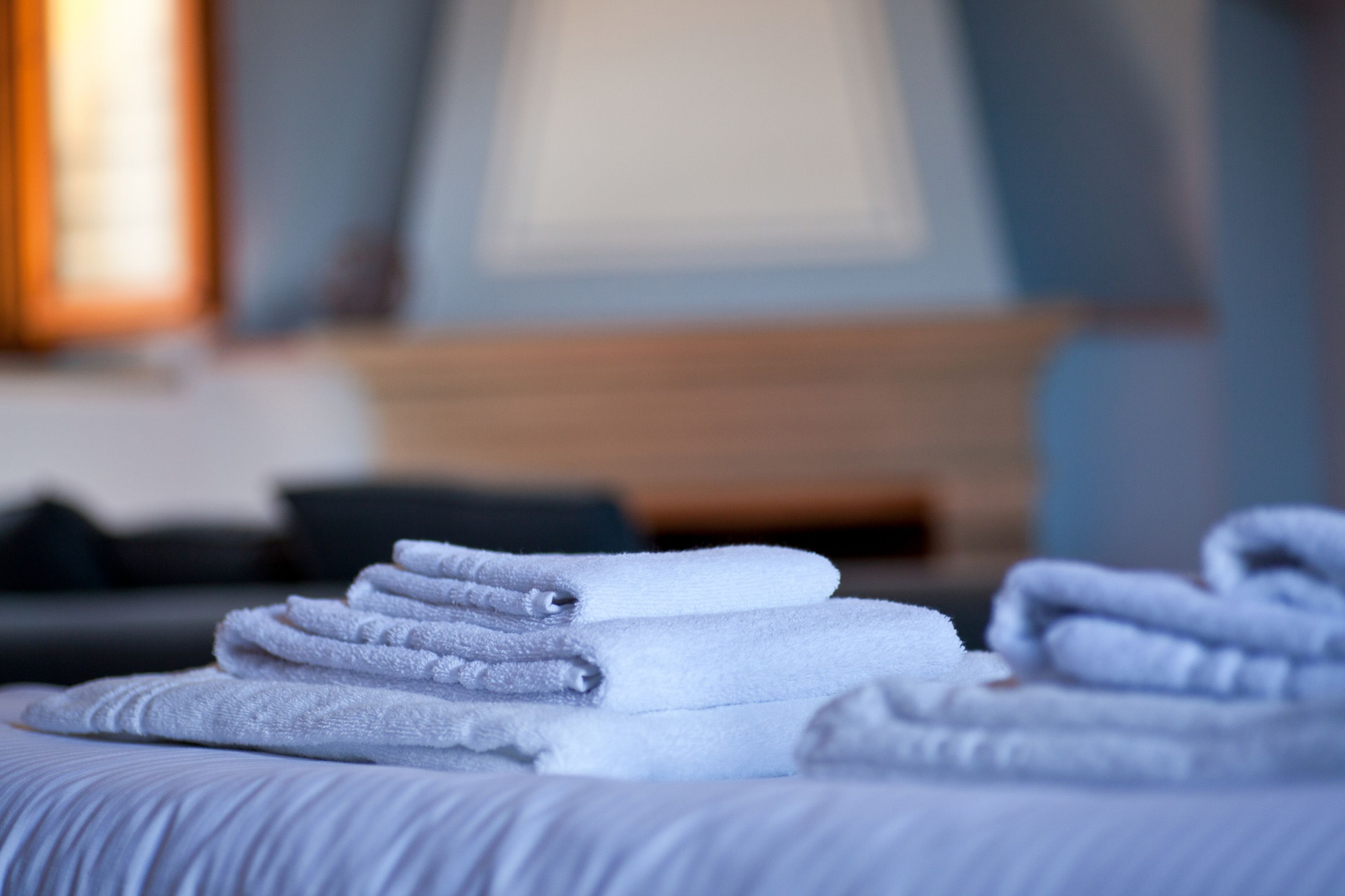 A neatly folded stack of white towels on a bed in a hotel room.