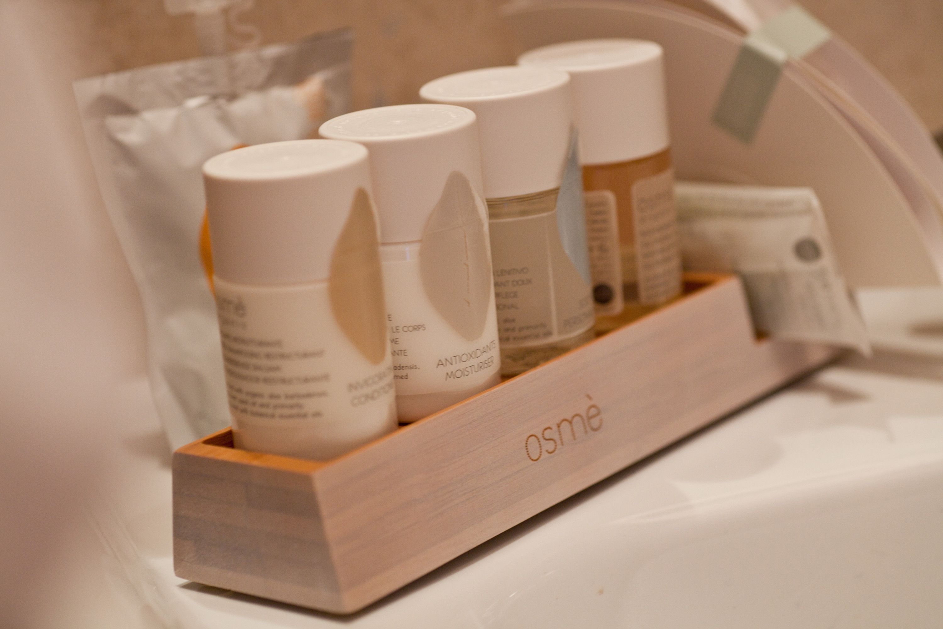 Un plateau en bois contenant plusieurs produits de soins pour la peau, chacun étant muni d’une étiquette, est posé sur une surface blanche.