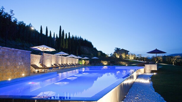 A swimming pool with lounge chairs and umbrellas, surrounded by stone walls and a landscaped area with trees. - Relais Villa Belvedere (Figline e Incisa Valdarno)