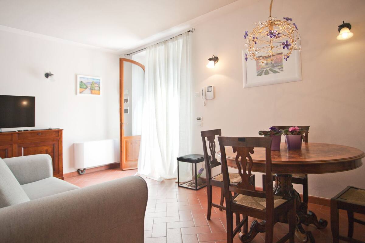 A living room with a TV, sofa, dining table with chairs, and a chandelier.
