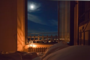 Un dormitorio con vistas a la ciudad de noche, una ventana y un radiador.