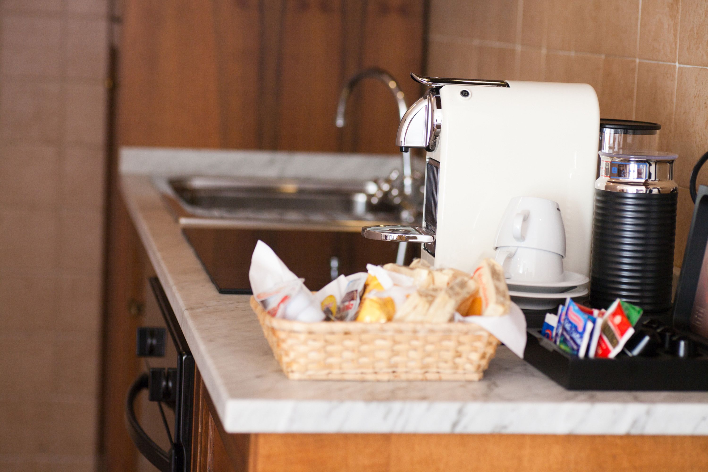 A kitchen with a coffee machine, a basket of bread, and a coffee pot on the counter.