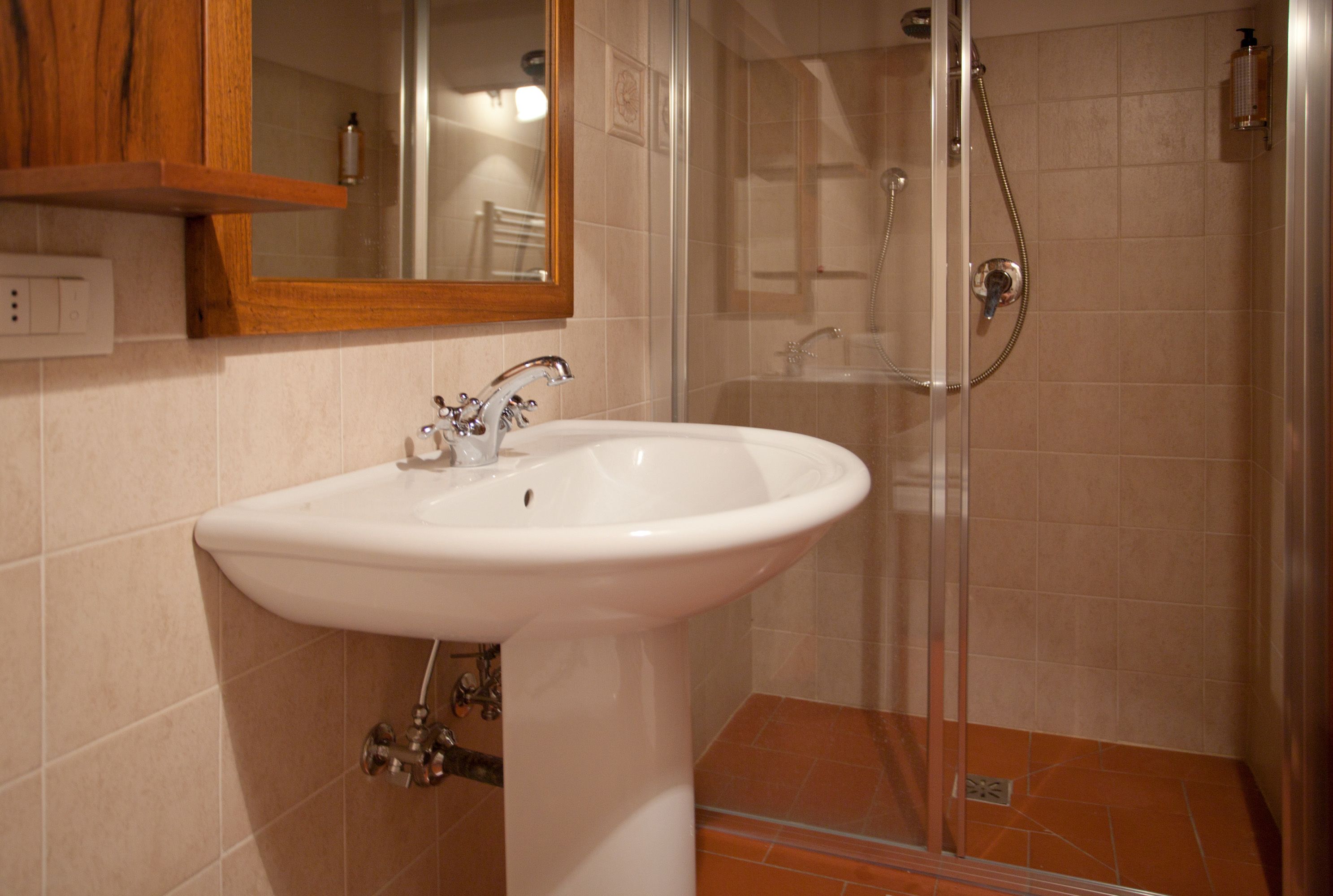 Ein Badezimmer mit einem weißen Waschbecken, einer Glasdusche und einem Holzschrank darüber.