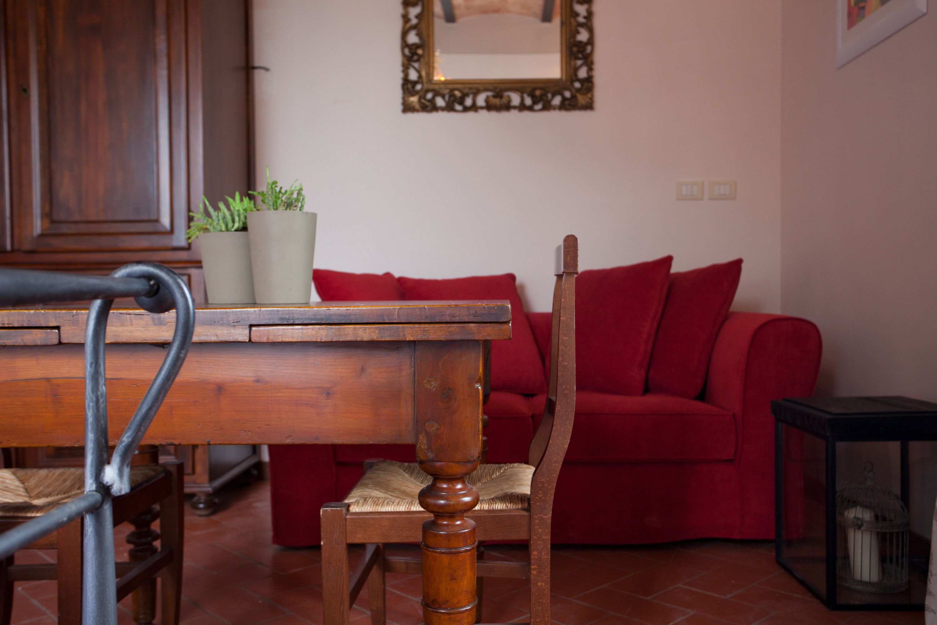 Una mesa de comedor de madera con sillas, un sofá rojo y plantas en macetas en una habitación con suelo de baldosas.