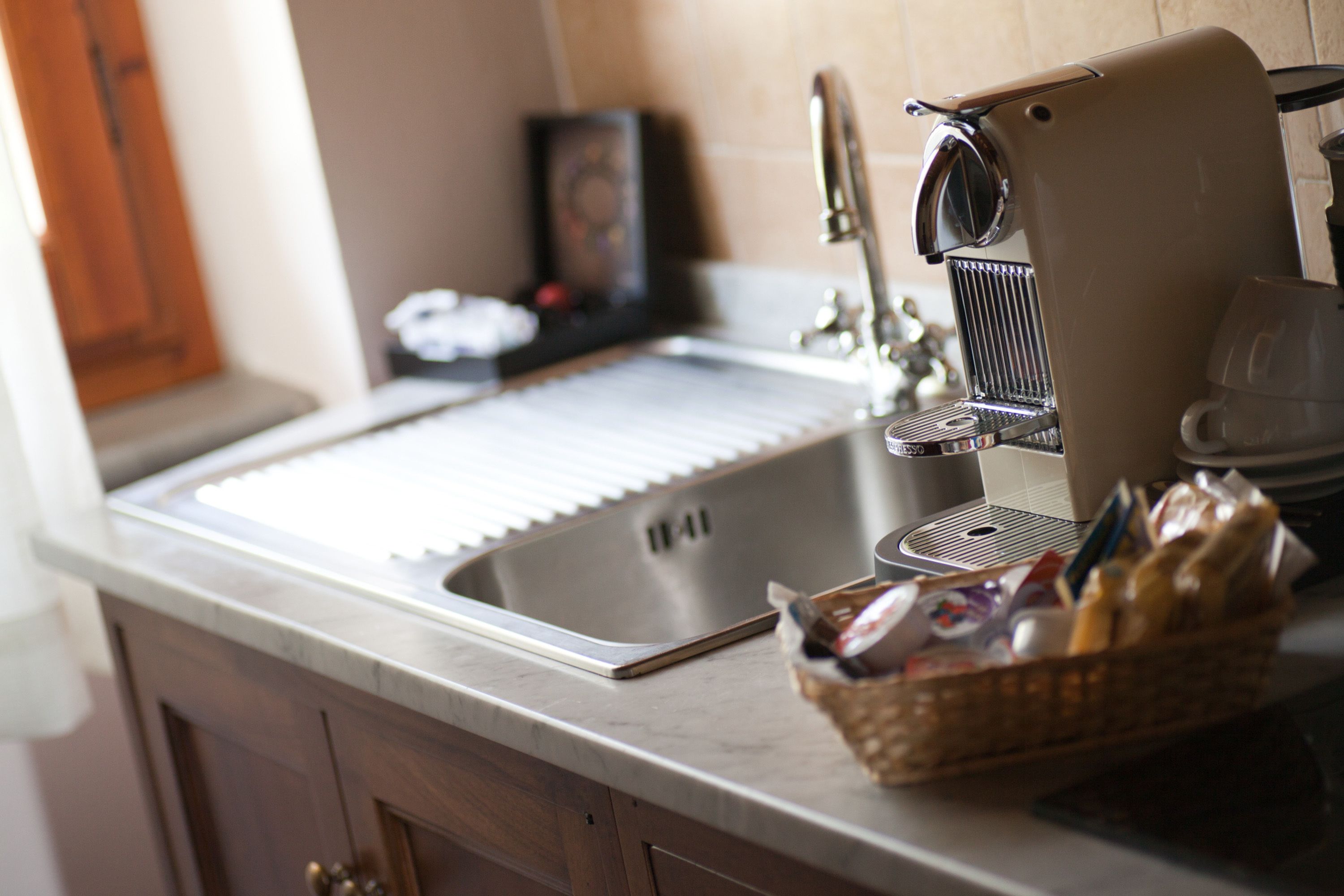 A kitchen with a stainless steel sink, a coffee machine, and a basket of bread.