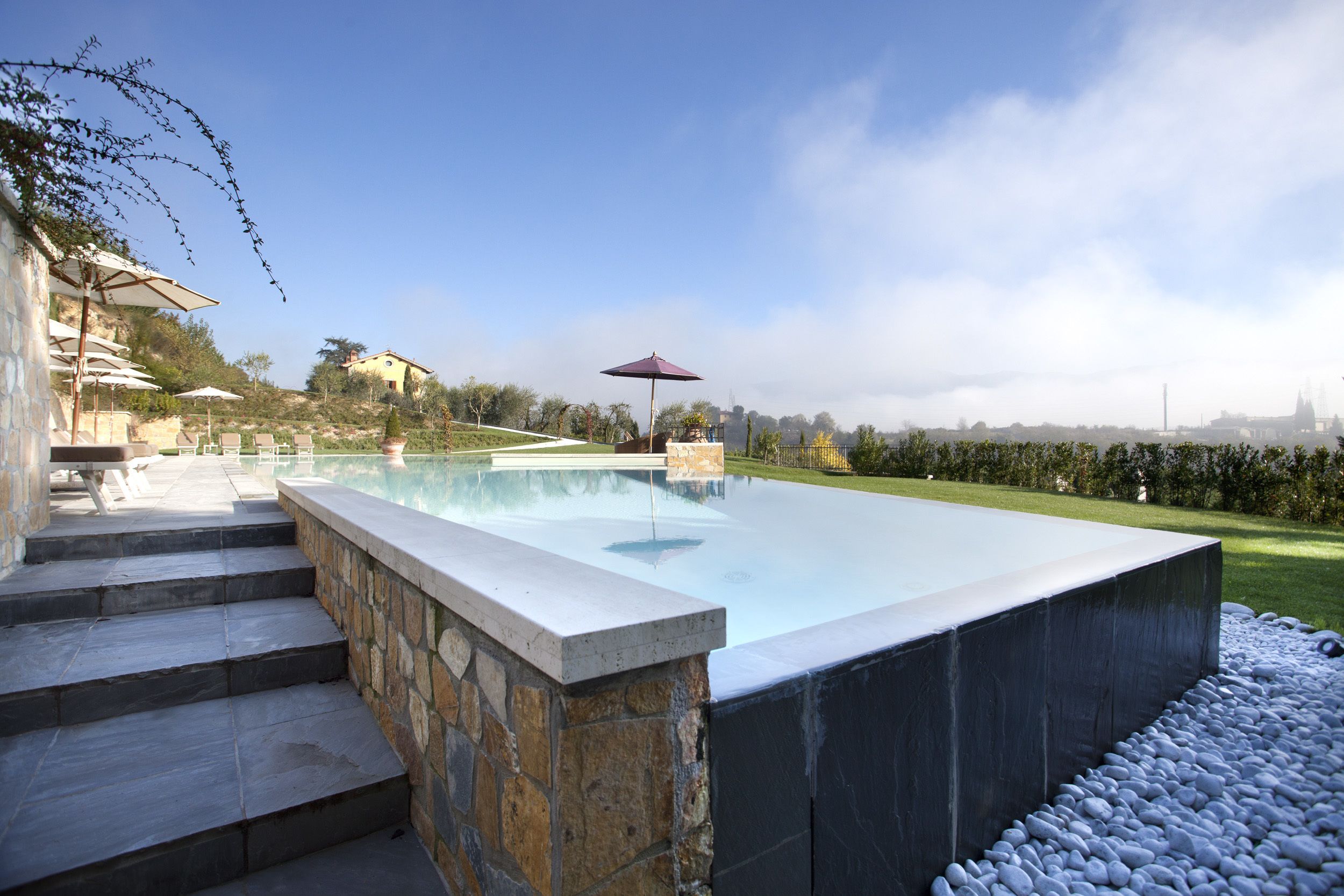 A swimming pool with steps leading up to it, surrounded by stone walls and a grassy area.