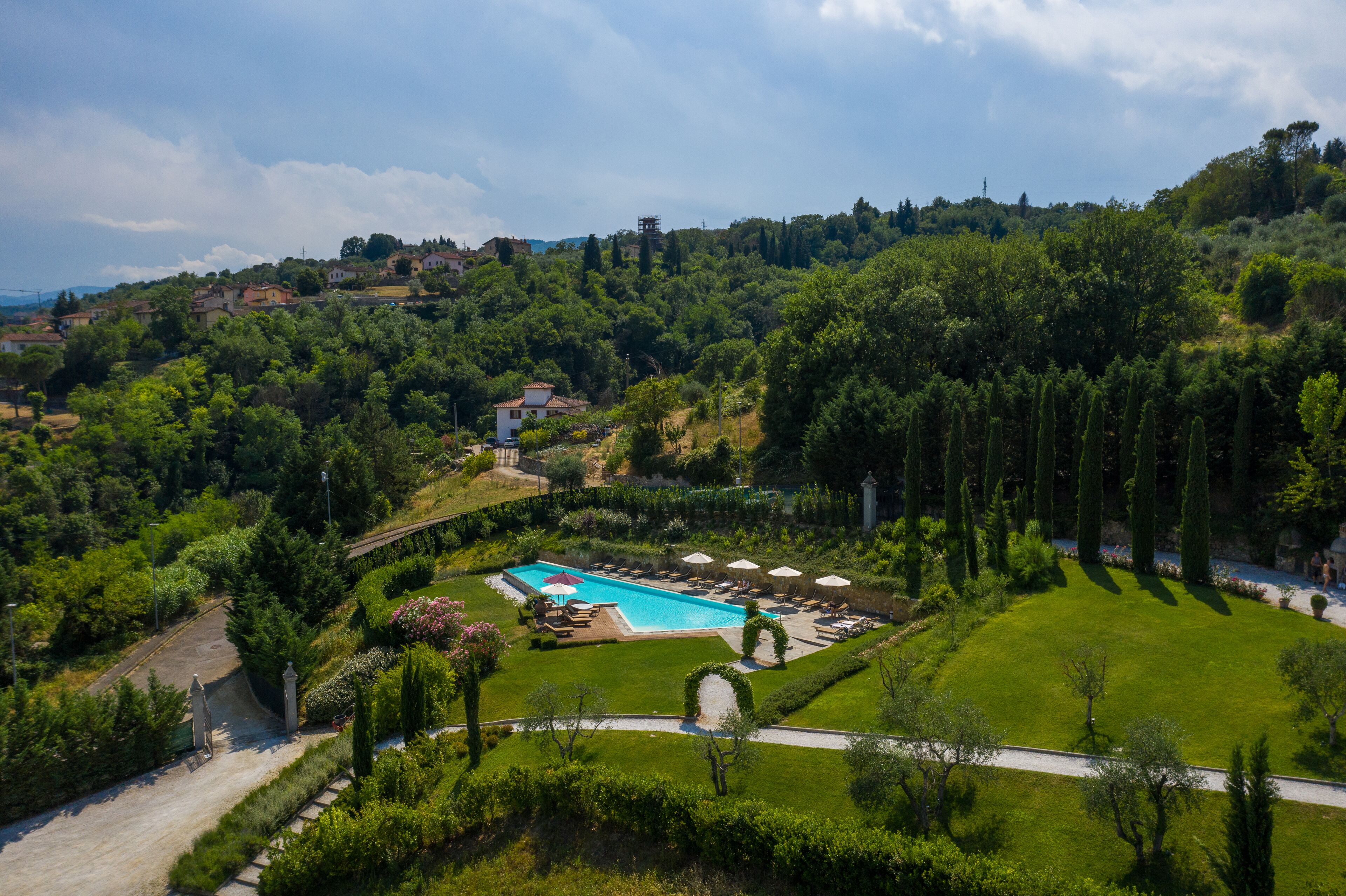 Una grande piscina circondata da prati curati e alberi, con vista su un paesaggio collinare sullo sfondo.