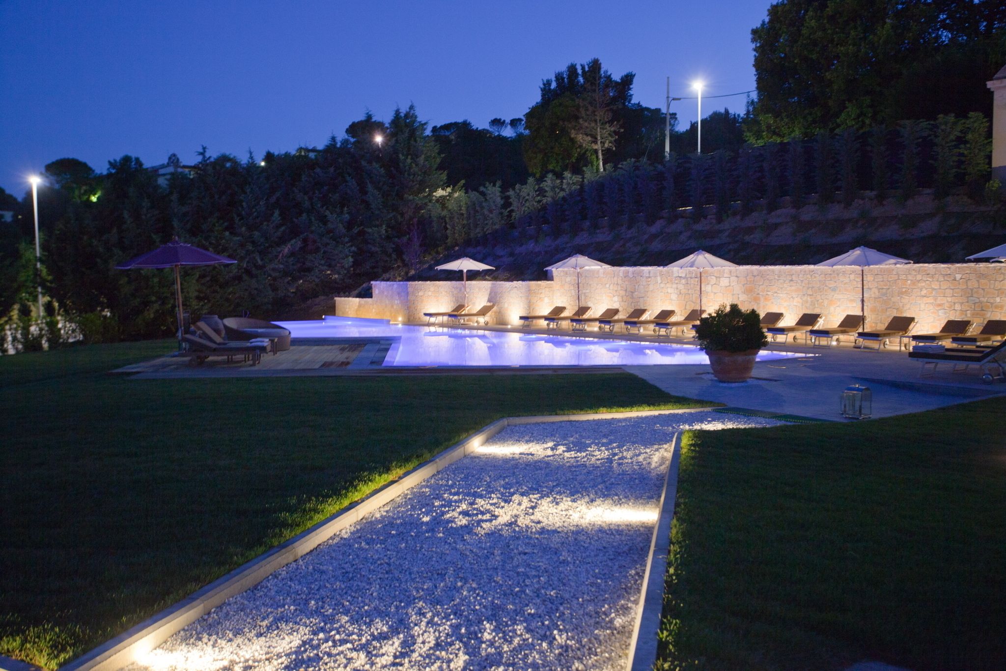 Un espace piscine aménagé avec des chaises longues et des parasols, entouré d’un mur de pierre et de verdure.
