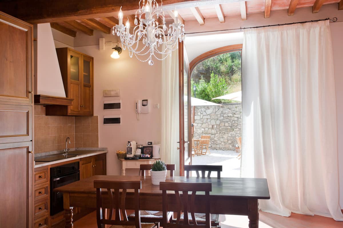 A kitchen with wooden cabinets, a dining table with chairs, a chandelier, and a view of the outside.