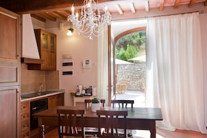 Una cocina con armarios de madera, una mesa de comedor con sillas, una araña y vistas al exterior a través de un ventanal.