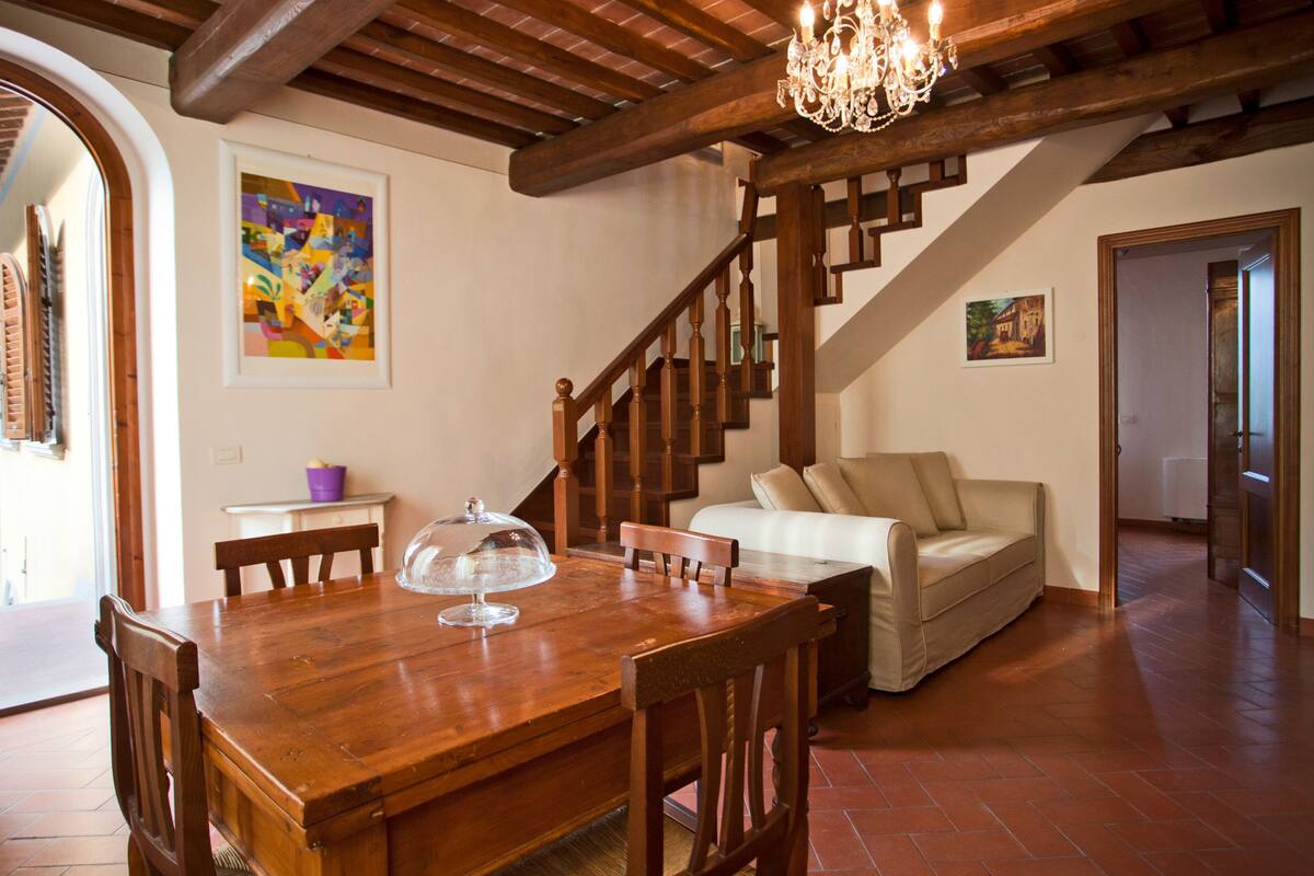 A dining area with a wooden table and chairs, a chandelier, and a staircase leading to another room.