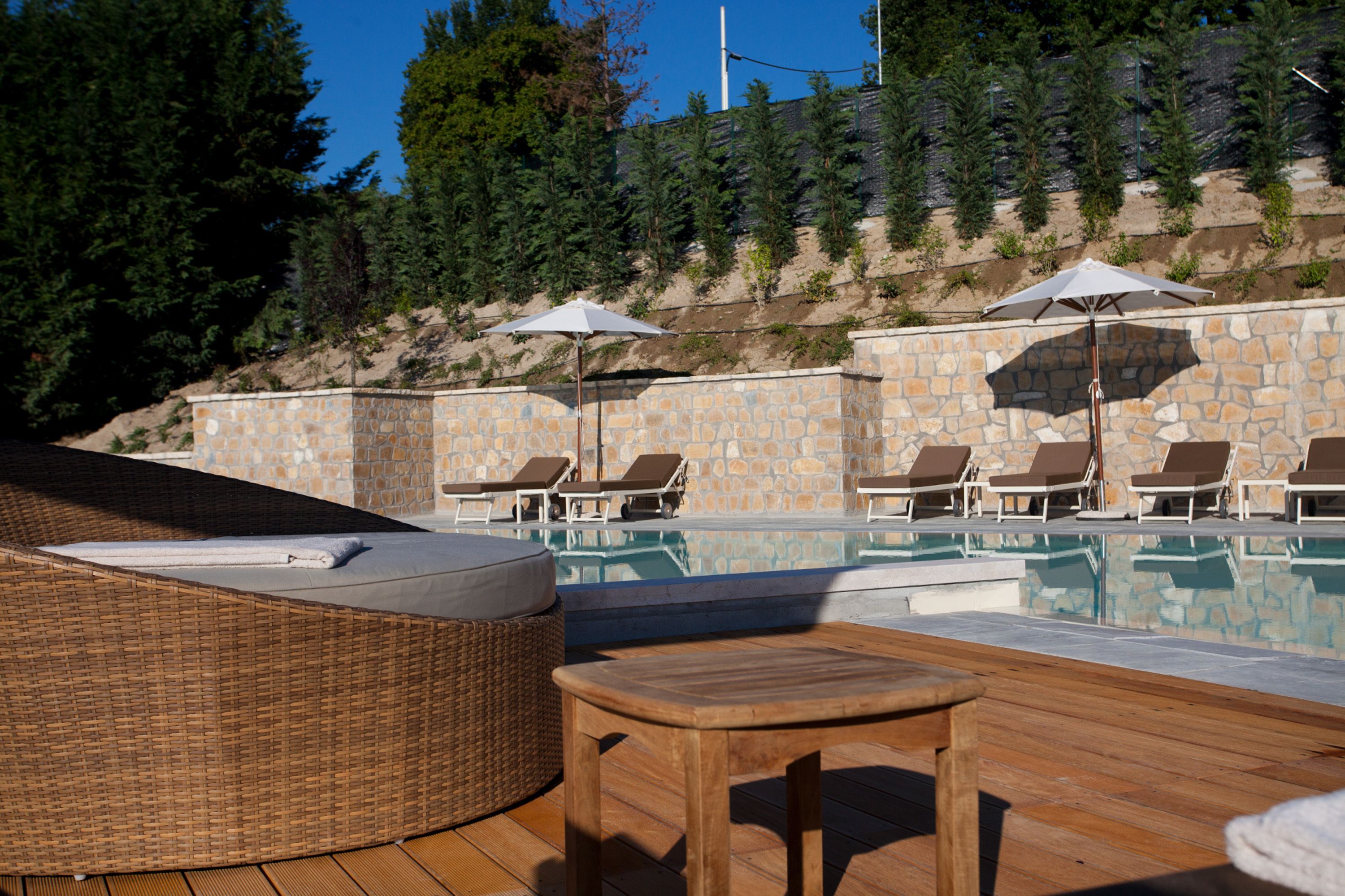 A pool area with lounge chairs and umbrellas, surrounded by stone walls and trees.