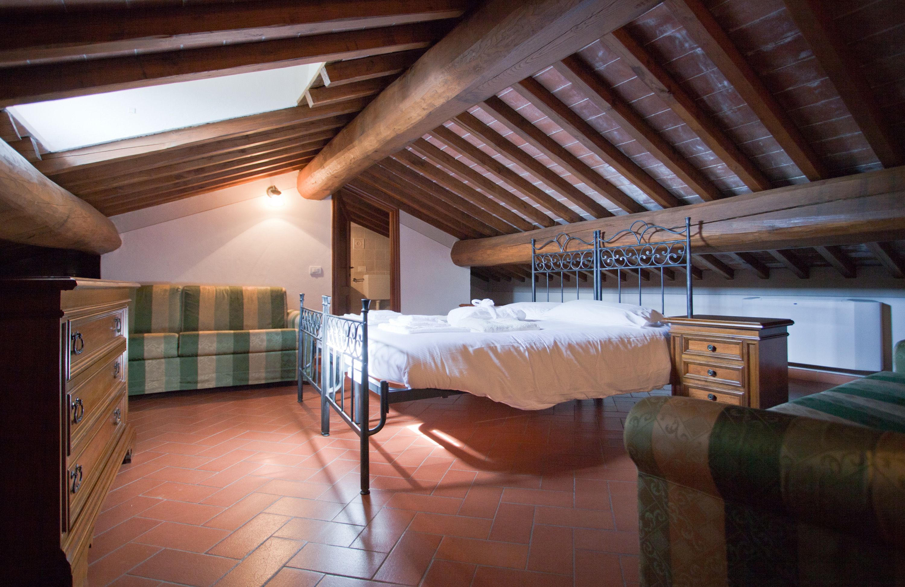 Une chambre avec un plafond en bois, un lit recouvert de draps blancs, un canapé à rayures vertes et une commode en bois.