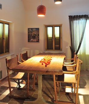 Une salle à manger avec une table et des chaises en bois, un tableau au mur et des fenêtres avec des rideaux.