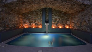 A stone-walled hot tub with two champagne glasses, a stone arch ceiling, and a small waterfall feature.