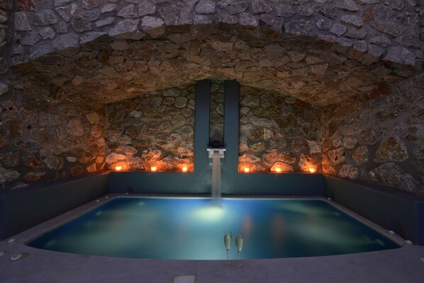 Un bain à remous aux murs de pierre, agrémenté de deux coupes à champagne, d’une voûte en pierre et d’une petite cascade décorative.