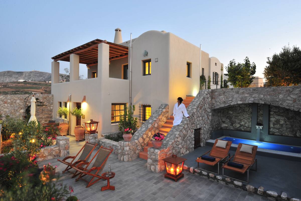 Una casa moderna con fachada de piedra, una escalera de piedra y mobiliario exterior con sillones de descanso.