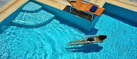 A swimming pool with a wooden deck and lounge chairs.