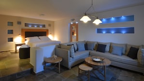 A modern hotel room with a bed, sofa, two small tables, and a ceiling light fixture.