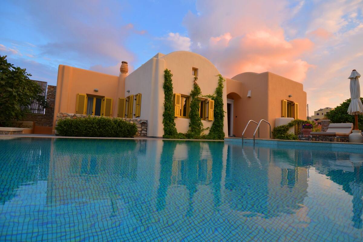 Vista de una piscina frente a un edificio de estilo mediterráneo, con paredes de piedra y contraventanas amarillas.