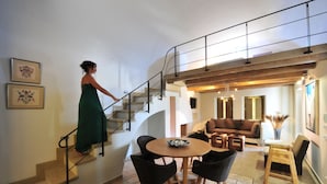 A woman descending a staircase in a modern interior with a dining area, sofas, and artwork.