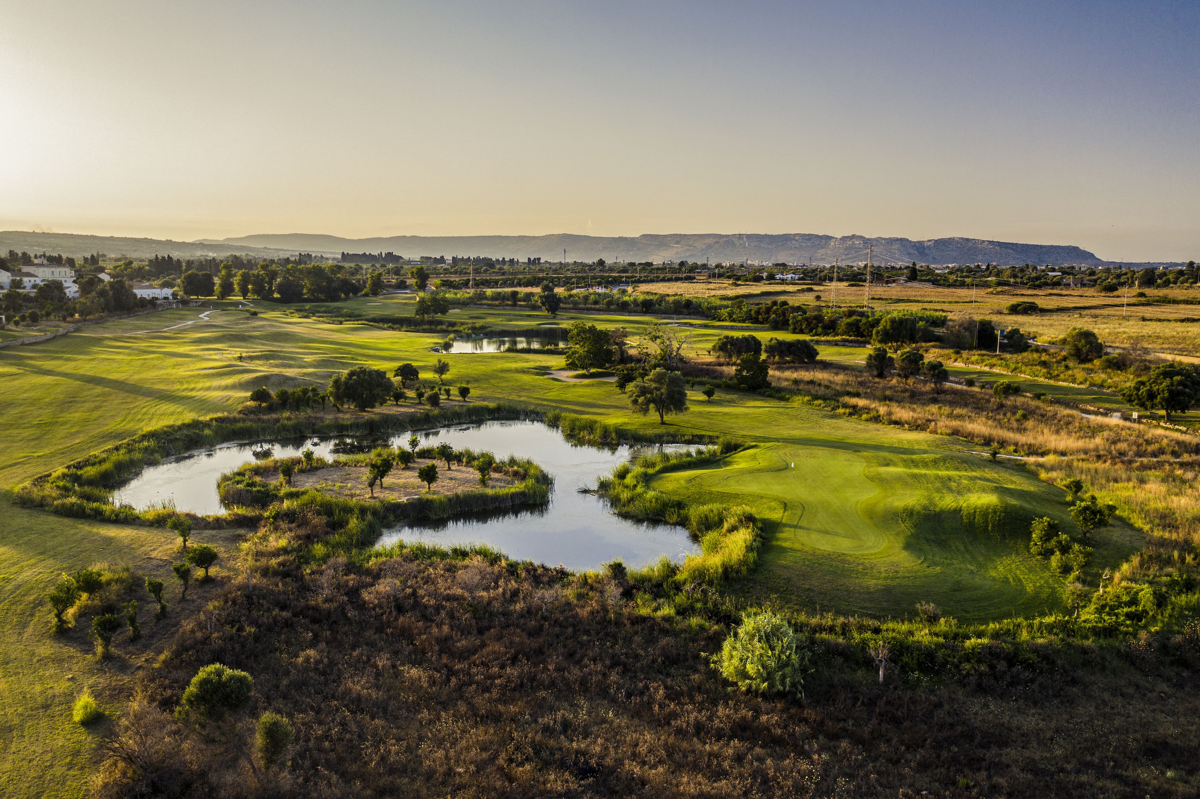 A golf course with a pond, trees, and distant mountains.