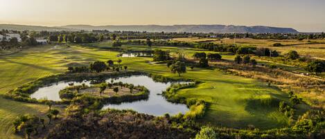 A golf course with a pond, trees, and distant mountains.
